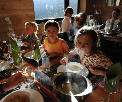 Famiglia seduta al tavolo ben apparecchiato di una capanna mangia una zuppa fumante