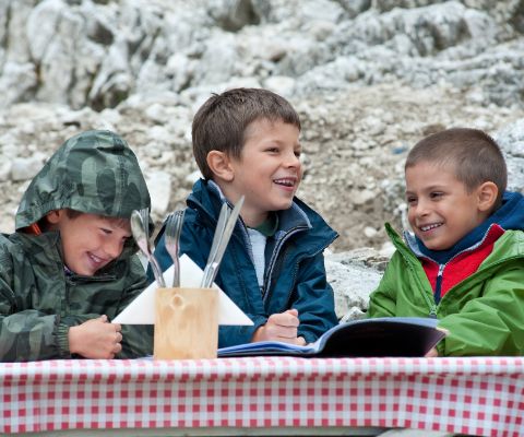 Trois garçons assis rient à une table sur une terrasse dans les montagnes