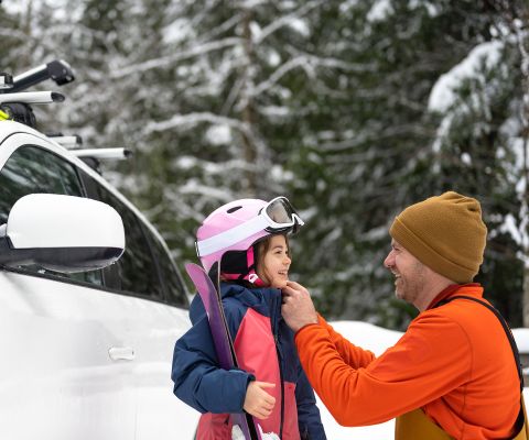 Un père enfile le casque de ski sur la tête de sa fille.