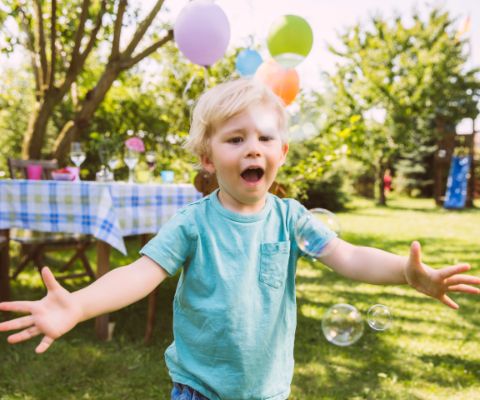 Bambino a una festa in giardino rincorre delle bolle di sapone