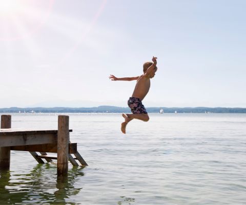 Garçon sautant dans un lac depuis une passerelle