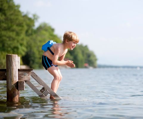 Kleiner Junge mit Schwimmhilfe macht sich bereit zum Sprung in den See