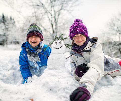 Kinder freuen sich über den Winter und bauen einen Schneemann