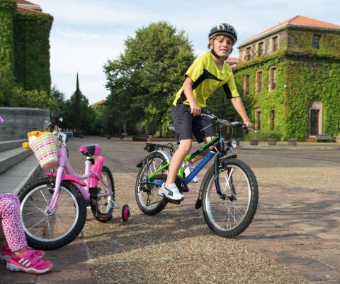 Ragazzo su una bici e ragazzina seduta su una scala, davanti a lei una bici da bambini