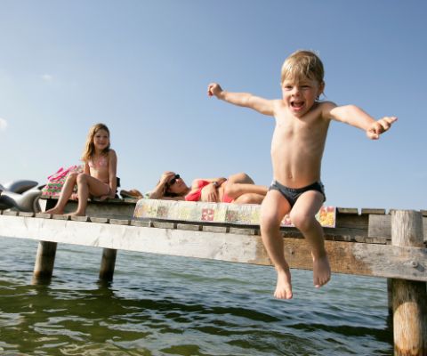 Familie liegt auf Holzsteg und Junge springt lachend ins Wasser