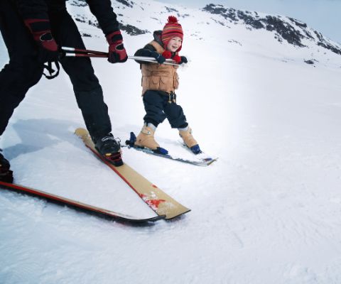 Kleines Kind lernt Skifahren und hält sich an Skistöcken fest