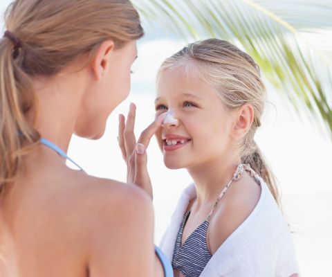 Donna in spiaggia mette la crema sul viso di una bambina