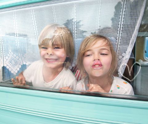 Kinder schauen aus dem Wohnwagen hinter dem Vorhang hervor 