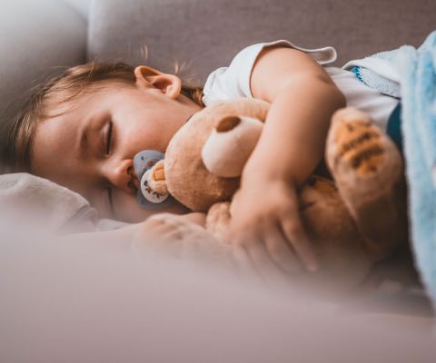 Kind schläft mit Teddybär im Arm
