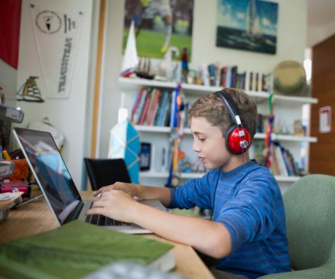 Un garçon avec des écouteurs écrit sur un ordinateur portable
