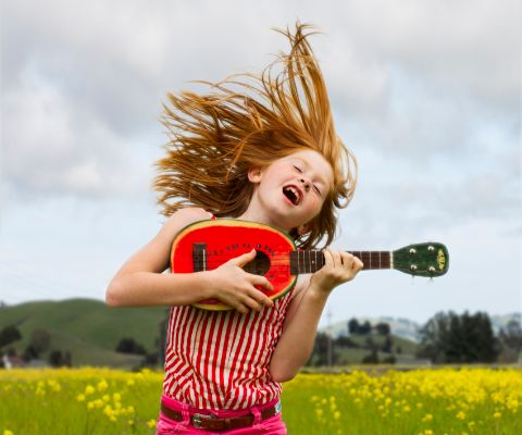 Mädchen vor Wiese hüpft und spielt auf Kindergitarre
