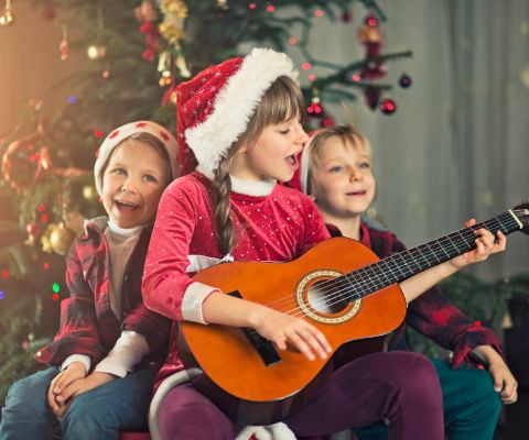 Drei Kinder vor dem Weihnachtsbaum singen und spielen Gitarre