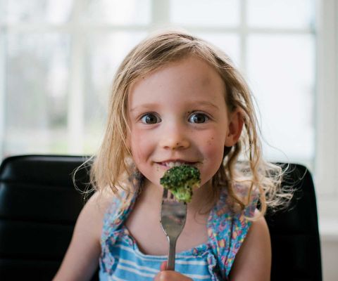 Consigli contro lo spreco alimentare: bambina che mangia broccoli 