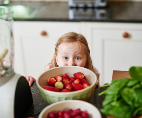 Kleines Mädchen in einer Küche, vor ihr eine Schüssel mit Erdbeeren