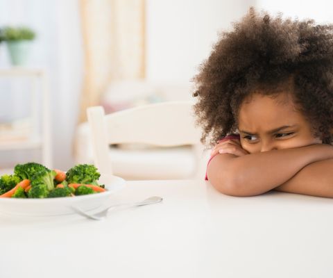 Ein Kind schaut misstrauisch auf einen Teller mit Gemüse