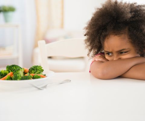 Una bambina che guarda con sospetto un piatto di verdure