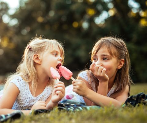 Due bambine mangiano un gelato sedute sul prato 
