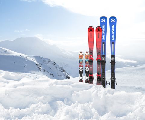 Trois paires de skis plantés dans la neige devant un paysage hivernal