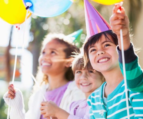 Kinder feiern mit farbigen Ballonen und Hüten