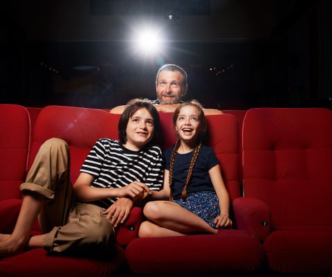 Un homme et deux enfants regardent, captivés, un écran de cinéma
