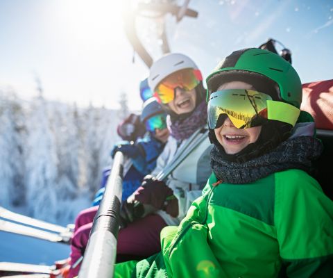 Familie in Skiausrüstung sitzt lachend im Skilift
