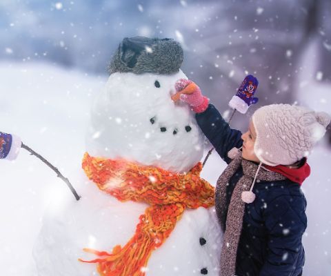 Un bambino attacca una carota a un pupazzo di neve per fare il naso