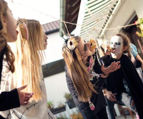 Divertimento di Halloween: delle bambine cercano di mangiare donut appesi a un cordoncino