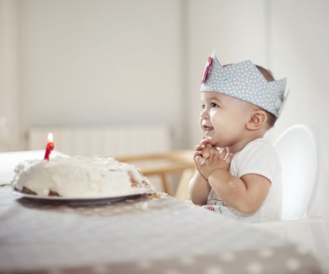 Un bébé est assis dans sa chaise haute devant un gâteau d’anniversaire avec une bougie
