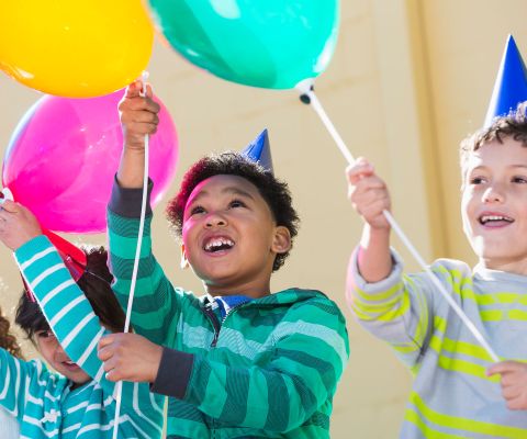 Tre bambini festeggiano un compleanno e tengono in mano dei palloncini