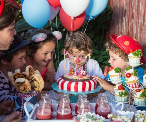 Devant une table joliment décorée, des enfants font de grands yeux devant un superbe gâteau d’anniversaire