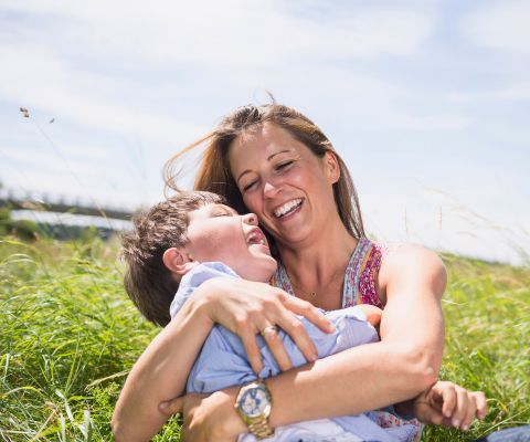 Assise dans un pré, une mère souriante tient son petit garçon dans les bras