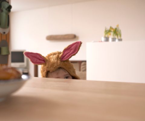 Un bambino mascherato da coniglio guarda oltre il bordo di un tavolo