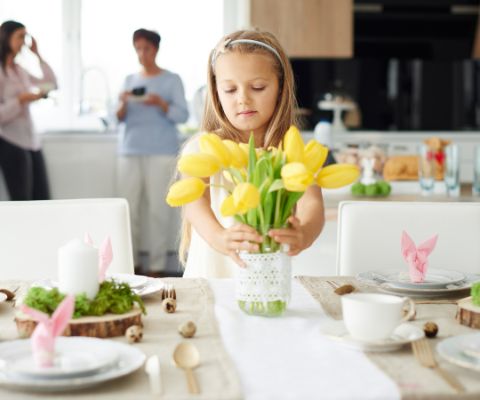 Una bambina poggia dei tulipani freschi su una tavola decorata con motivi pasquali