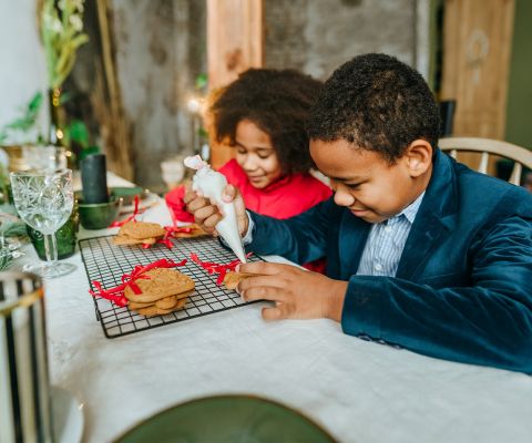 Deux enfants décorant des biscuits de Noël avec une poche à douille