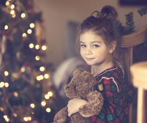 Mädchen mit Teddybär vor dem Weihnachtsbaum