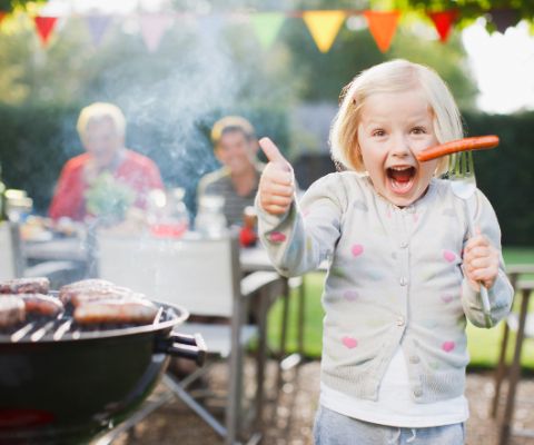 Bambino con salsiccia di fianco a un grill da giardino Bambino con salsiccia di fianco a un grill da giardino