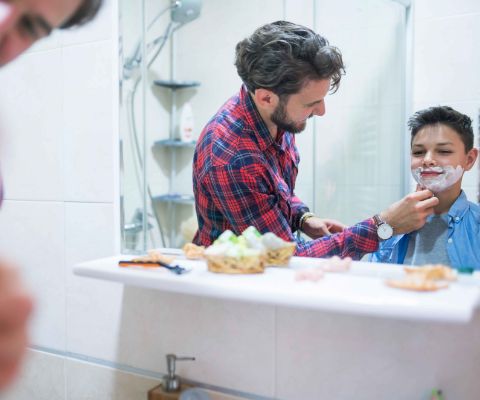 Vater hilft dem Sohn beim Rasieren des ersten Bartwuchses 