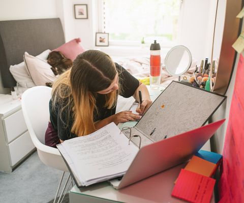 Une adolescente est assise à son bureau avec un classeur ouvert et écrit