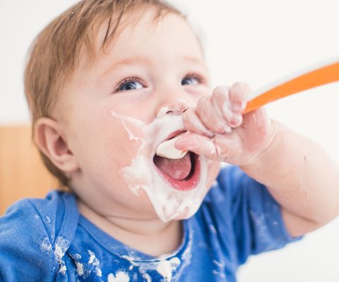Un bebè mangia uno yogurt con un cucchiaio per bebè