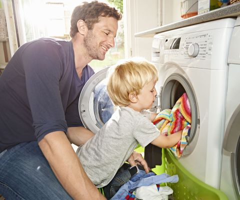 Un père vide la machine à laver avec son fils.