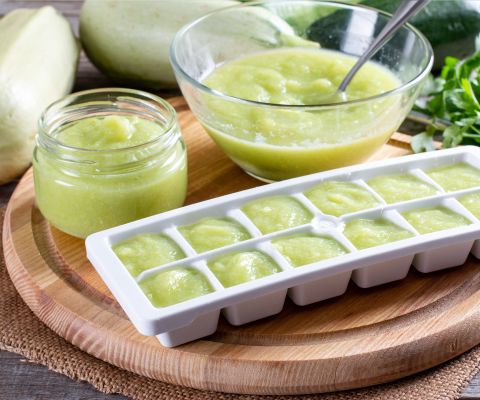 Grüner Babybrei wird in Eiswürfelbehälter zum Einfrieren gefüllt