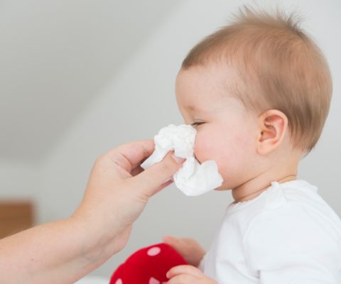 Bebè che si soffia il naso in un fazzolettino tenuto dalla mamma