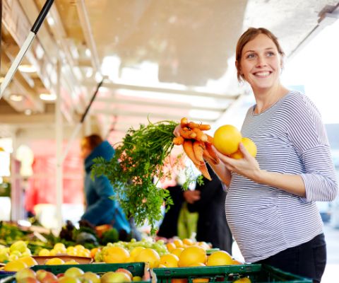 Femme enceinte souriante au supermarché en train de tenir des légumes dans ses mains