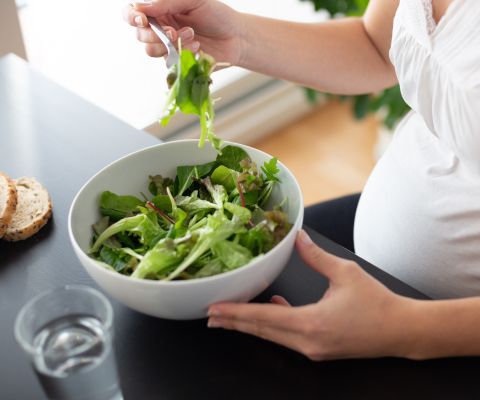 Una donna incinta seduta a un tavolo mangia un'insalata
