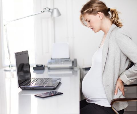 Femme enceinte assise à un bureau et se tenant le dos