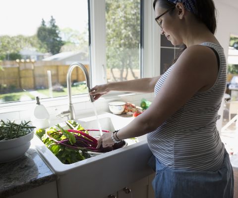 Femme enceinte en train de laver des légumes dans la cuisine