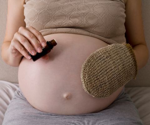 Schwangere pflegt ihren Babybauch mit Sisalhandschuh und Öl