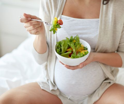 Une femme enceinte, un bol à la main, mange de la salade.