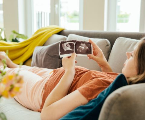 Liegende schwangere Frau schaut auf Ultraschallbilder ihres Babys