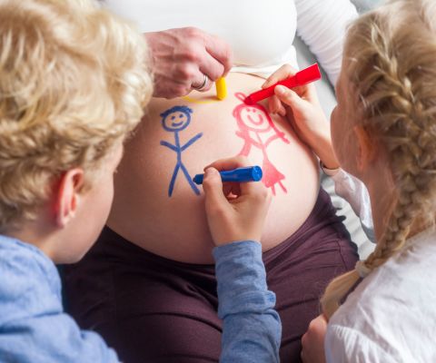 Una bambina piccola e un ragazzo pitturano la pancia di una donna incinta
